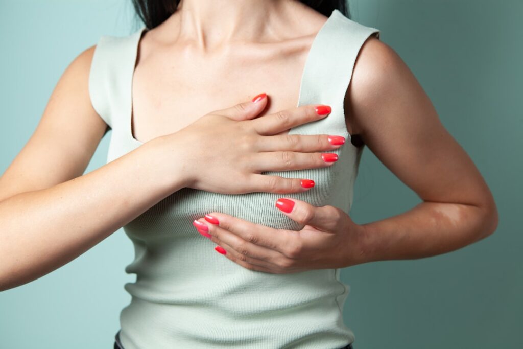 ACP Updates Breast Cancer Screening Guidelines for Women Woman performing breast self-examination against a teal background.