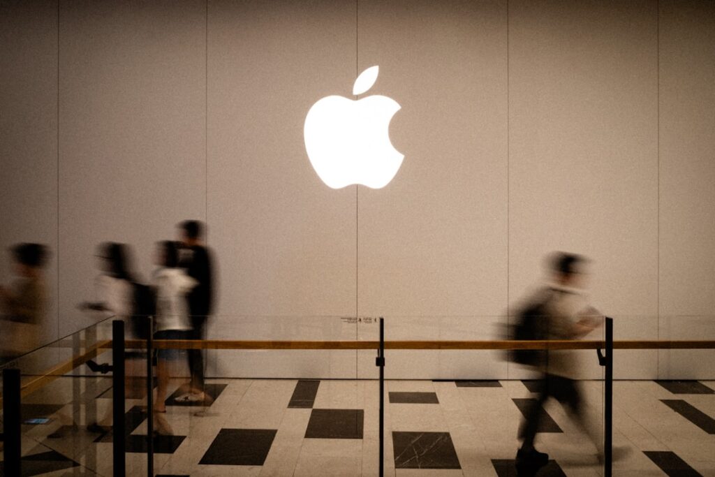 Apple Names John Ternus as New CEO, Cook Becomes Chair People walk past a large glowing apple logo.
