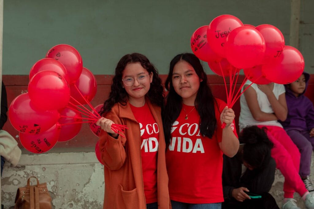 World Hemophilia Day 2026: Diagnosis as Gateway to Care Two girls are holding red heart shaped balloons