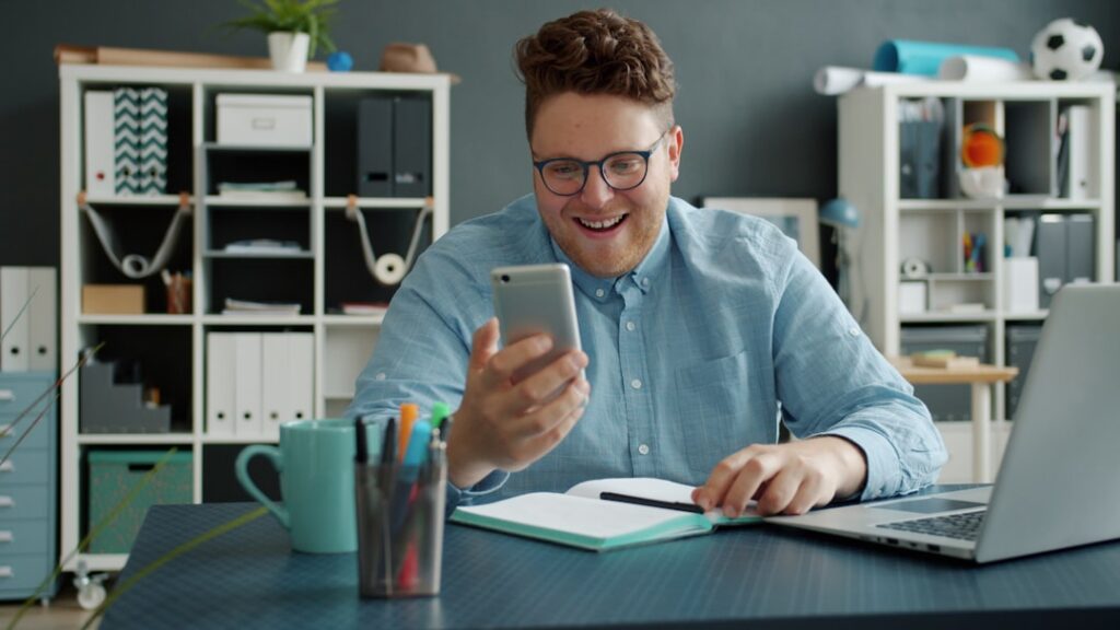Young CEO's Mindset Drives $11B Startup Valuation Man smiling while looking at his phone at desk