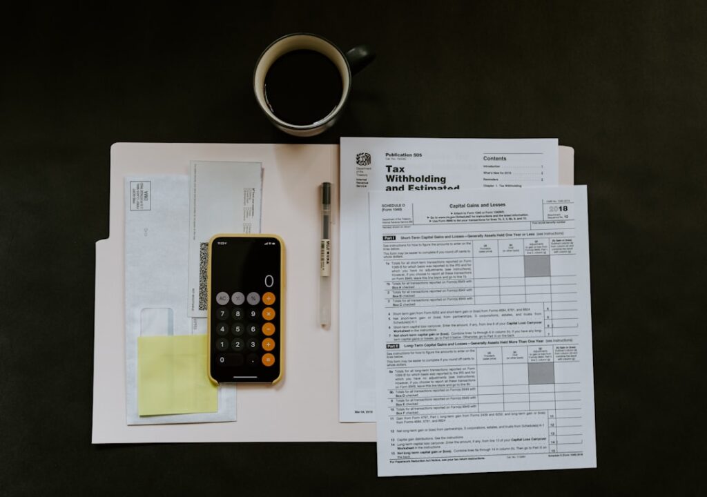 Self-Employment Tax Guide: Rates, Rules & Deductions black Android smartphone near ballpoint pen, tax withholding certificate on top of white folder
