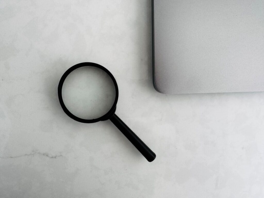 Getting Your Brand Into AI Search Results Magnifying glass sits near a laptop on a table.