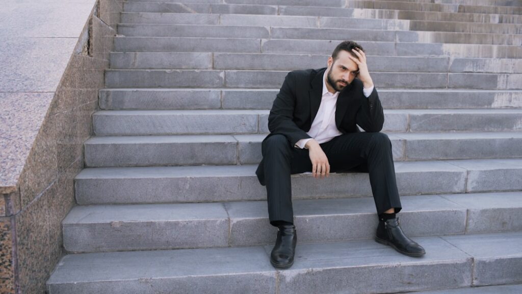 Can Founder Mode Leadership Actually Last Long-Term? Man in suit sitting on outdoor stairs looking down.