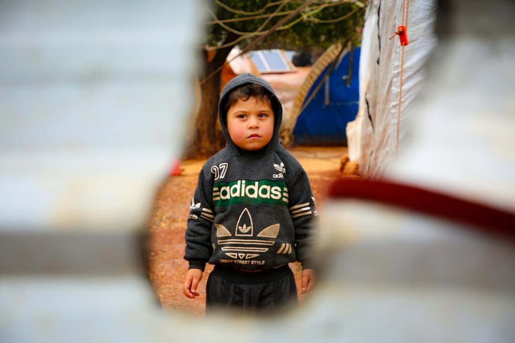 Child Poverty in Wales Reaches Crisis Level at 33% A young boy in a black adidas jacket looking through a hole in a wall