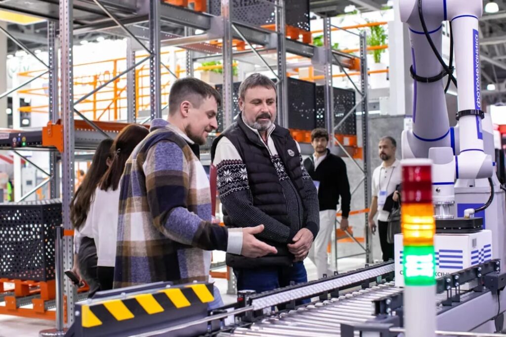 Dematic GreyOrange Partnership Transforms Warehouse Automation Men observe automated conveyor belt system in warehouse