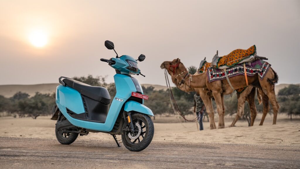 Iran Conflict Driving Up Energy, Food, and Living Costs Scooter and camels in the desert at sunset.