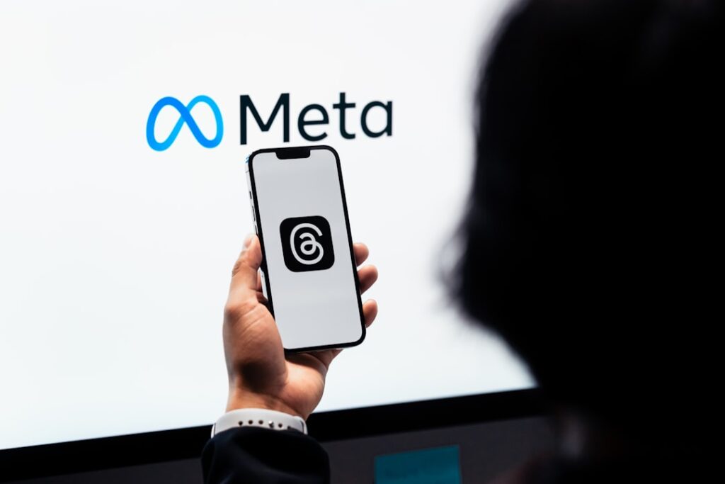 Meta to Cut 8,000 Jobs Amid AI Investment Push a person holding a cell phone in front of a large screen