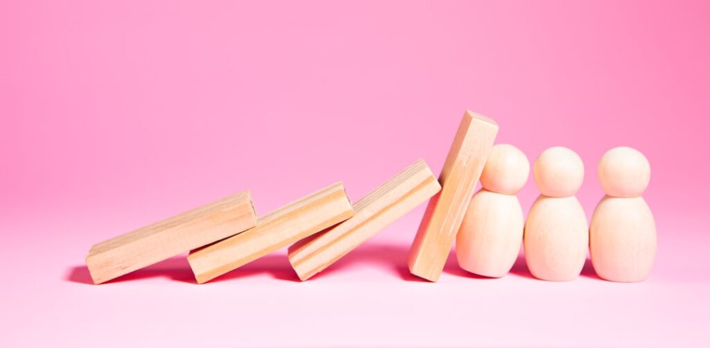 When Optimism Becomes Your Blindspot in Business Wooden blocks falling towards small figures on pink background