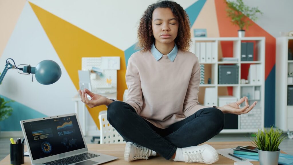 Employee Wellness Programs Drive Business Growth Woman meditating at a desk with laptop.