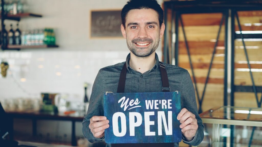 Franchise Search Guide: 10 Critical Steps to Success Barista holds an "open" sign, welcoming customers.