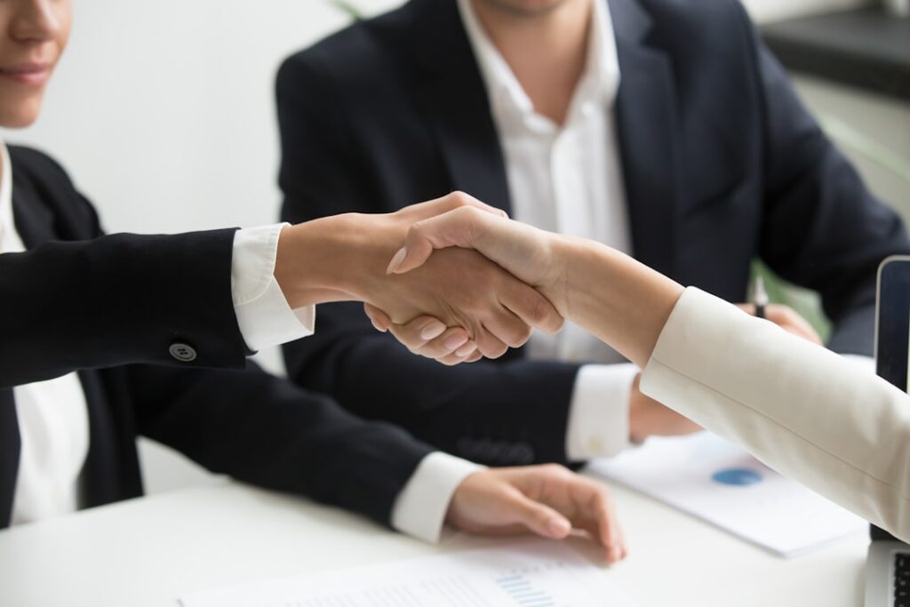 Shareholder Rights at Risk in RMAX, KALV, GBTG Deals two people shaking hands in front of a laptop