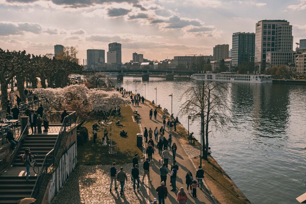 Sun Life Q1 2026 Earnings Beat Expectations People stroll along a riverfront promenade with city buildings.