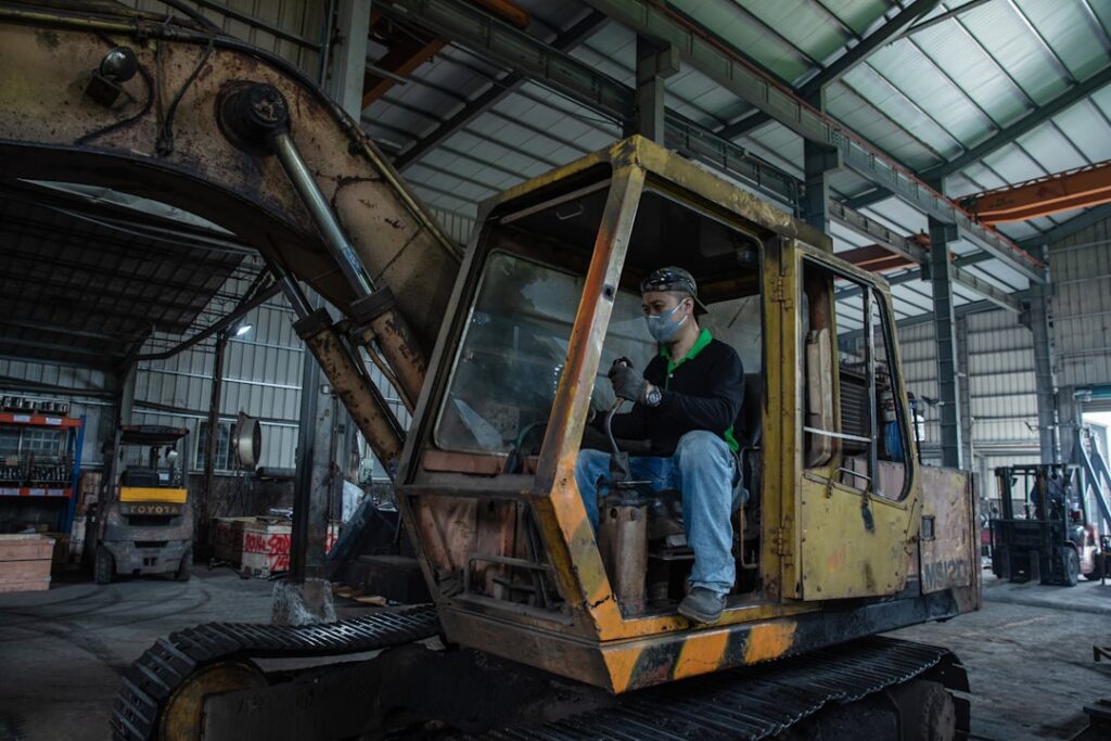 XCMG Secures Global Top 3 Ranking in 2026 Yellow Table Man sits in an old excavator in a workshop.
